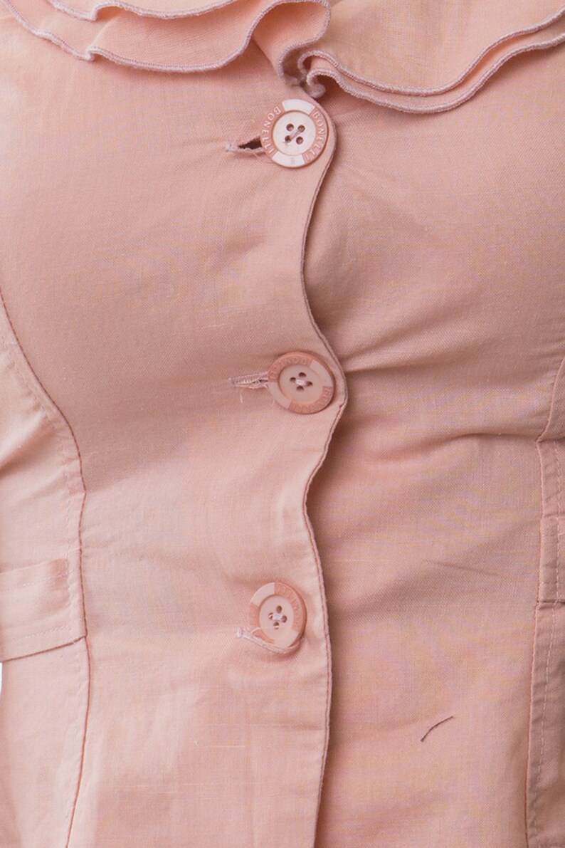 May include: A light pink button-down shirt featuring a ruffled collar and three circular buttons down the front. Each button is embossed with the text BONELLI. The garment is constructed from a solid-colored fabric with visible vertical seams.