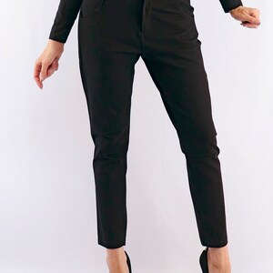 May include: Black trousers with a button closure and pockets. The pants are paired with black high heels. The outfit is all black, creating a sleek and streamlined look. The trousers appear to be made of a smooth fabric.