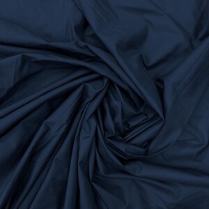 May include: A solid dark navy blue fabric with a smooth, matte texture. The material is gathered and draped in a swirling, circular pattern, creating deep shadows and highlights across the folds of the textile surface throughout the image.