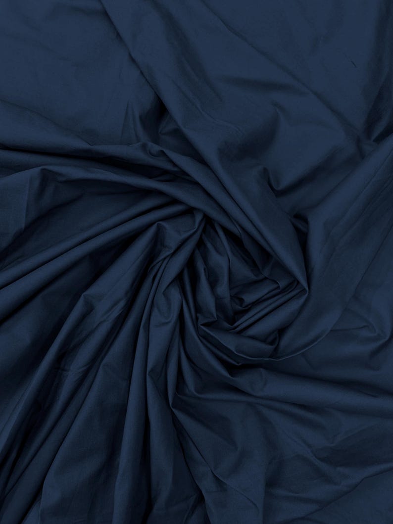 May include: A solid dark navy blue fabric with a smooth, matte texture. The material is gathered and draped in a swirling, circular pattern, creating deep shadows and highlights across the folds of the textile surface throughout the image.