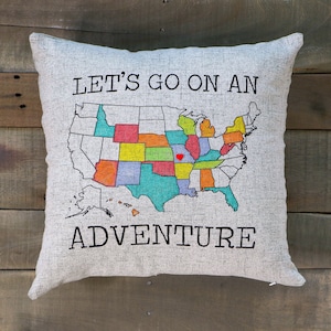 18x18 pillow sham with a zippered opening at the bottom. The sham is a soft faux linen texture and a light gray/taupe color. The front features a screen-printed US Map outline and the words Let's Go On An Adventure printed in black ink.