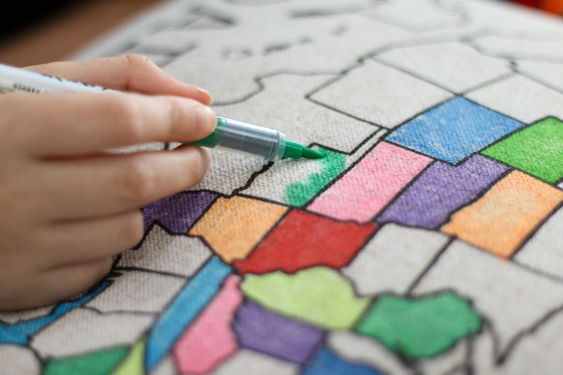 A video showing how to color your pillow sham in. Take light strokes on the top layer of the fabric. You build up the color with a light application. The example shows a hand with a green marker coloring in the state of Oklahoma.