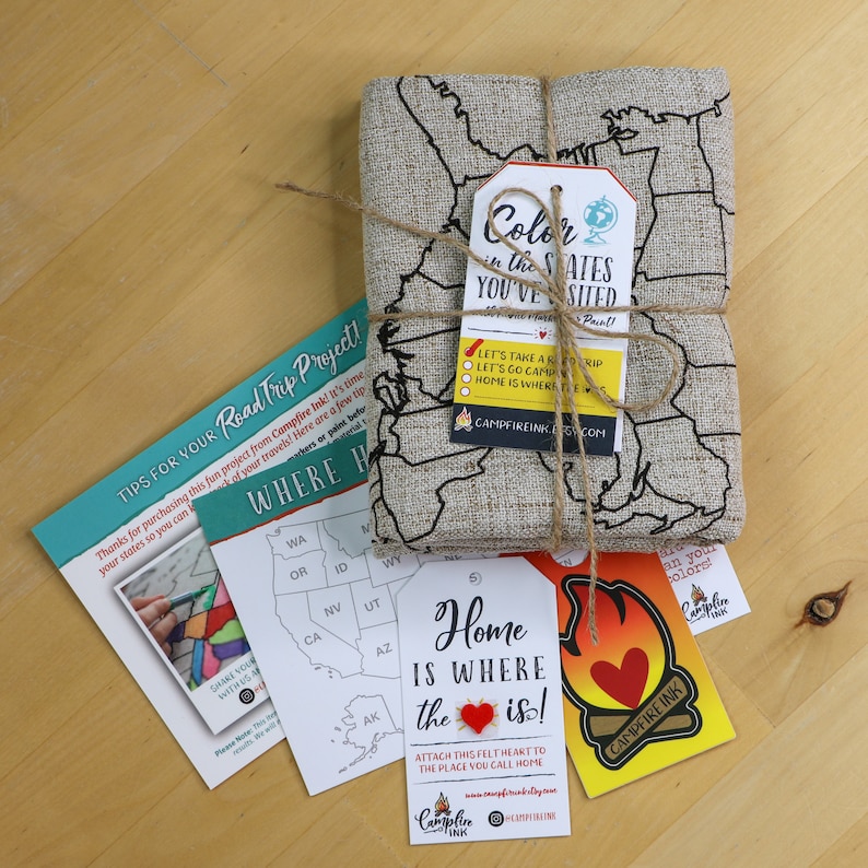 K&ouml;nnte beinhalten: Ein Bastelset f&uuml;r ein Roadtrip-Projekt. Das Set enth&auml;lt eine Karte der Vereinigten Staaten, ein Filzherz und ein Etikett mit der Aufschrift "Home is where the heart is!" Das Etikett ist an einem St&uuml;ck Schnur befestigt. Die Karte ist aus Jute und hat eine braune Schnur Schleife. Das Etikett ist gelb mit einem roten Herzen und dem Text "Campfire Ink".