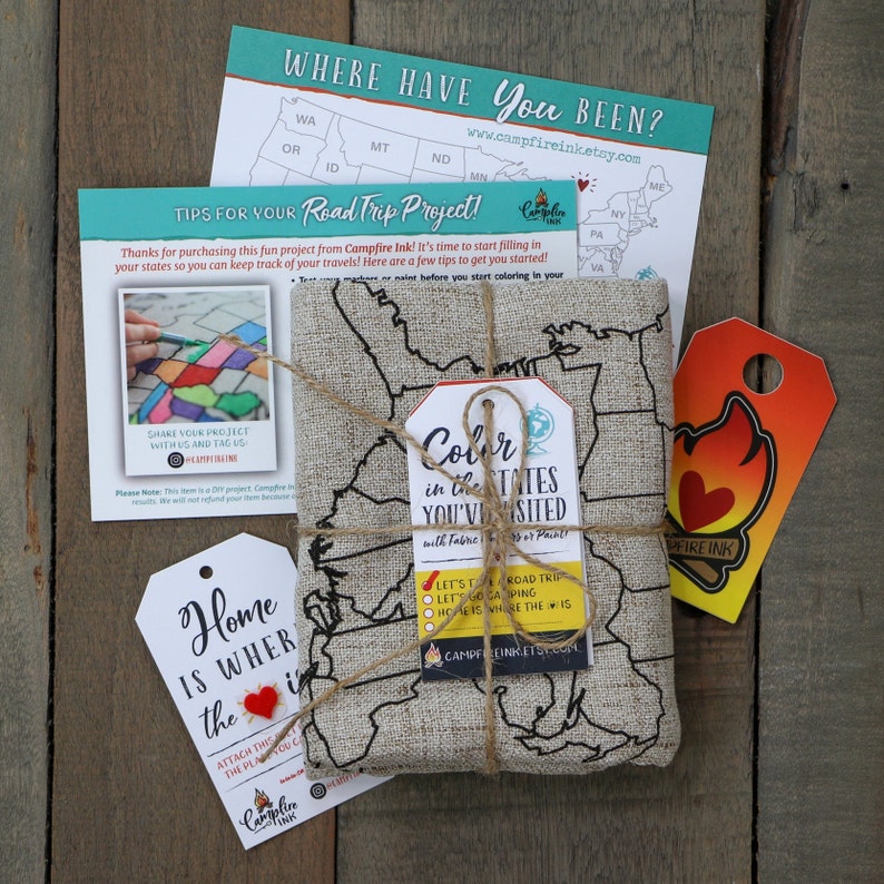 May include: A gift set for a road trip project. It includes a linen map of the United States, a tag that says "Color in the states you've visited", a tag that says "Home is where the "is", and a card with tips for the project. The set is wrapped in twine and tied with a small tag that says "Campfire Ink".