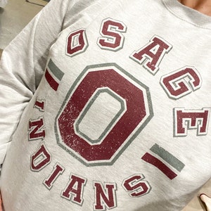 May include: Gray sweatshirt with a maroon and gray graphic of a large "O" inside a circle with the text "OSAGE INDIANS" around it.