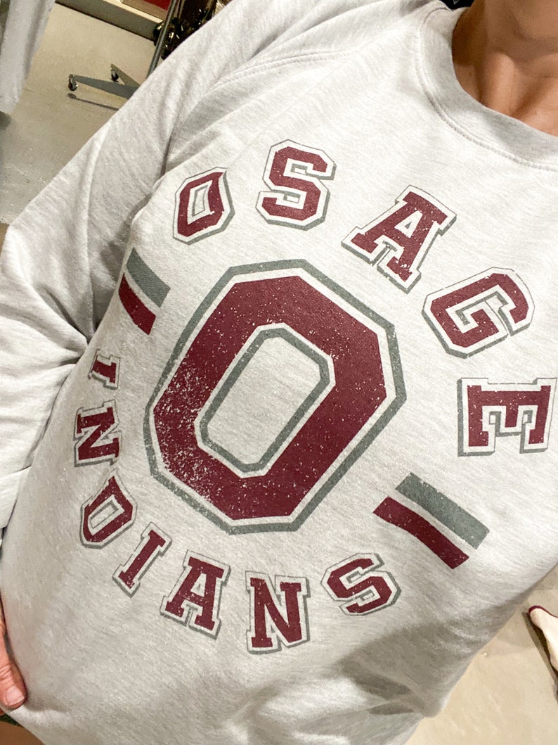 May include: Gray sweatshirt with a maroon and gray graphic of a large "O" inside a circle with the text "OSAGE INDIANS" around it.