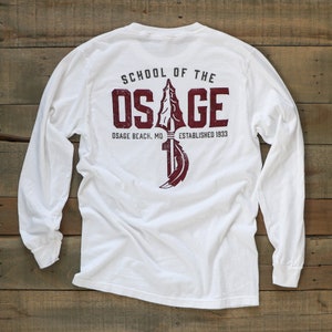 May include: White long-sleeve shirt with a maroon graphic on the back. The graphic includes the text "SCHOOL OF THE OSAGE" above an illustration of a spear and feather, with "OSAGE BEACH, MO ESTABLISHED 1933" below.