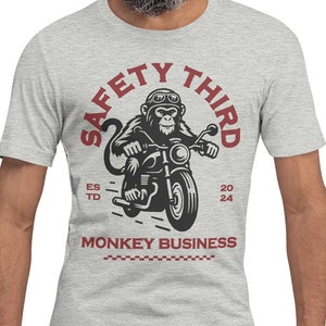May include: A gray t-shirt with a red and black graphic of a monkey riding a motorcycle. The graphic says "Safety Third" with "Est. 2024" below it. The text "Monkey Business" is below the graphic.