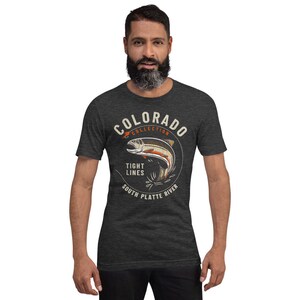 May include: A dark heather grey t-shirt with a vintage-style graphic of a trout jumping out of the water. The graphic includes the text "Colorado Collection", "Tight Lines", "South Platte River", and a red fishing lure.