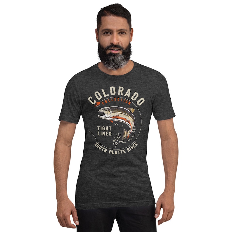 May include: A dark heather grey t-shirt with a vintage-style graphic of a trout jumping out of the water. The graphic includes the text "Colorado Collection", "Tight Lines", "South Platte River", and a red fishing lure.