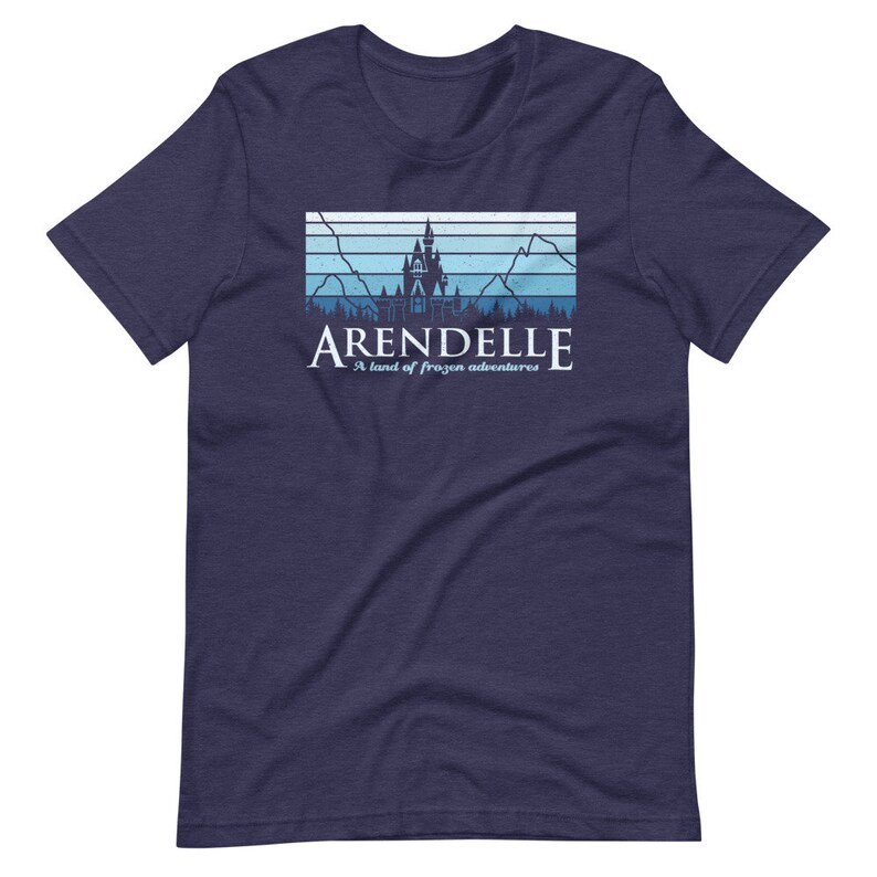 May include: A navy blue t-shirt with a retro-style graphic of a castle with mountains and trees in the background. The text "Arendelle" is printed below the graphic, along with the phrase "A land of frozen adventures".