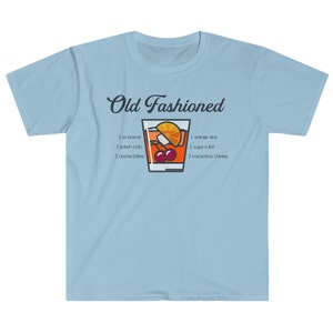 May include: Light blue t-shirt with a graphic of an Old Fashioned cocktail recipe. The recipe includes 2 oz brandy, 1 splash soda, 2 dashes bitters, 1 orange slice, 1 sugar cube, and 2 maraschino cherries.