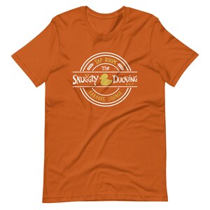 May include: Orange t-shirt with a white circle logo that says "Tap Room The Snuggly Duckling Karaoke Lounge" with a yellow rubber duck inside the circle.