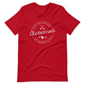 May include: Red short-sleeved t-shirt with a white circle graphic featuring the text "Lets Go Explore Wisconsin", crossed paddles, the state outline, and "The Badger State 18 48".