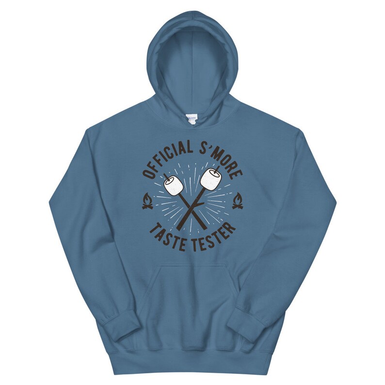 K&ouml;nnte beinhalten: Ein blauer Kapuzenpullover mit dem Text "OFFICIAL S'MORE TASTE TESTER" in einem kreisf&ouml;rmigen Design. Das Design umfasst gekreuzte Marshmallow-St&auml;be und kleine Lagerfeuer-Grafiken. Der Kapuzenpullover hat eine Vordertasche und eine Kapuze mit Kordelzug.