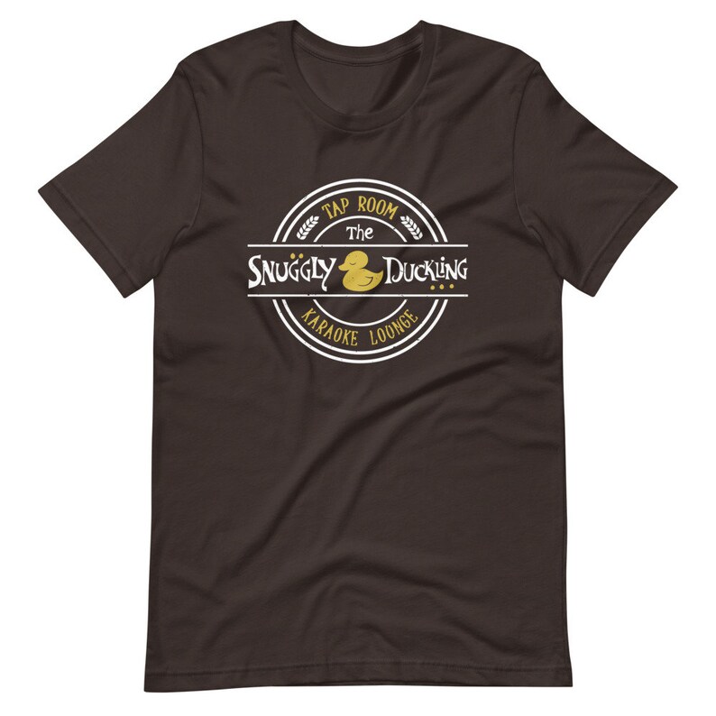 May include: A dark brown t-shirt with a white circle logo that says "The Snuggly Duckling Tap Room Karaoke Lounge" with a yellow rubber duck illustration.