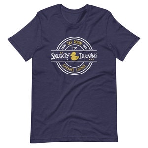 May include: A navy blue t-shirt with a white circle logo that says "The Snuggly Duckling Tap Room Karaoke Lounge" with a yellow rubber duck inside the circle.