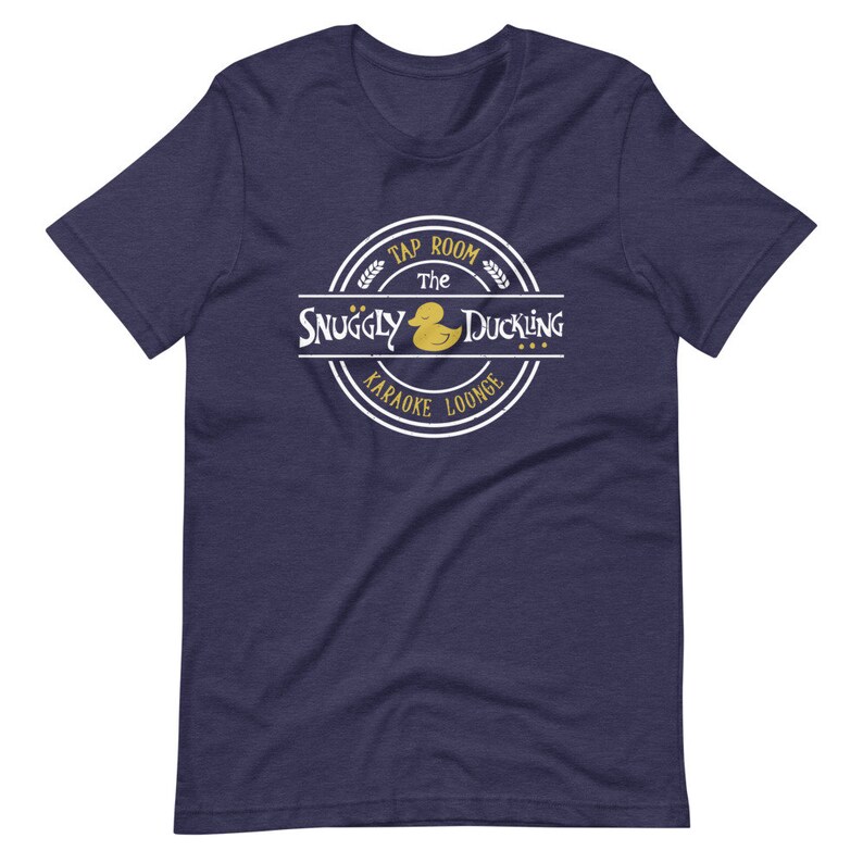 May include: A navy blue t-shirt with a white circle logo that says "The Snuggly Duckling Tap Room Karaoke Lounge" with a yellow rubber duck inside the circle.