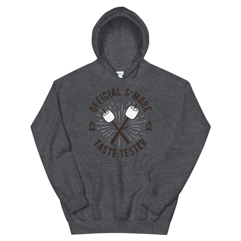 K&ouml;nnte beinhalten: Dunkelgrauer Kapuzenpullover mit Kordelzug. Auf der Vorderseite steht der Text "OFFICIAL S'MORE TASTE TESTER" in einem kreisf&ouml;rmigen Design mit gekreuzten Marshmallow-R&ouml;stst&auml;ben. Ein gem&uuml;tlicher Hoodie.