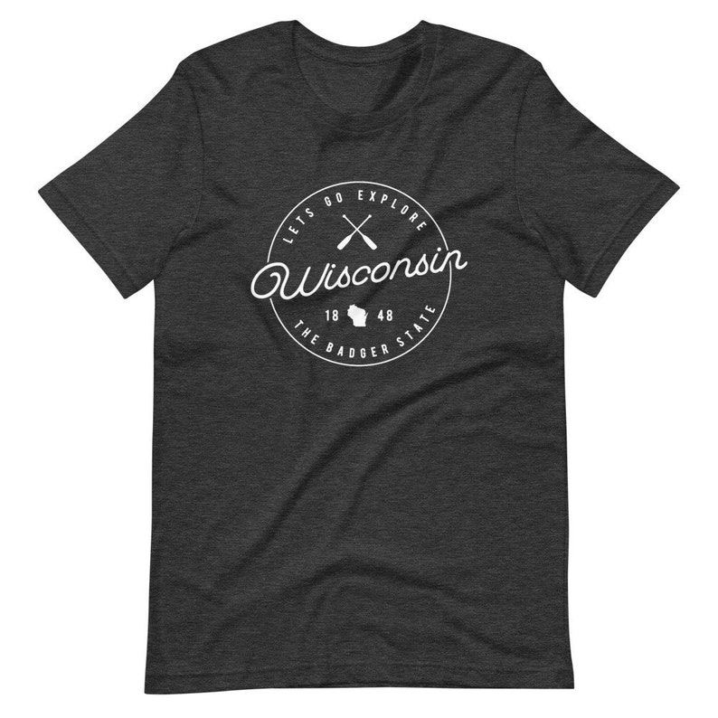 May include: A dark heather grey t-shirt with a white circle graphic featuring the text "Lets Go Explore Wisconsin", crossed paddles, the state outline, and "The Badger State 18 48".