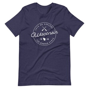 May include: Navy blue t-shirt with a white circle graphic that says "Let's Go Explore Wisconsin" with crossed paddles, a Wisconsin state outline, and "The Badger State" with the numbers 18 and 48.