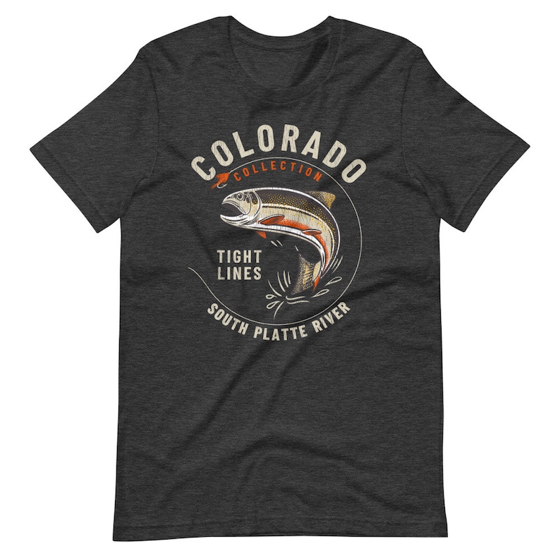 May include: A dark heather grey t-shirt with a vintage-style illustration of a trout jumping out of the water. The illustration is surrounded by a circle with the text "Colorado Collection", "Tight Lines", and "South Platte River".