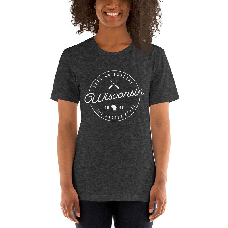May include: A dark heather grey t-shirt with a white circle graphic that says "Let's Go Explore Wisconsin" with a crossed paddle design and the text "The Badger State" with the state outline and the numbers 18 and 48.