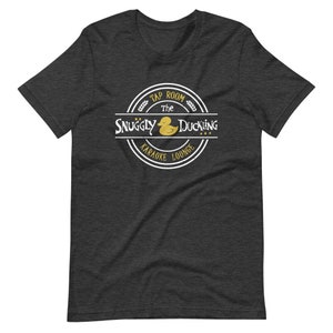 May include: A dark heather grey t-shirt with a white circle logo featuring a yellow rubber duck and the text "The Snuggly Duckling Tap Room Karaoke Lounge".