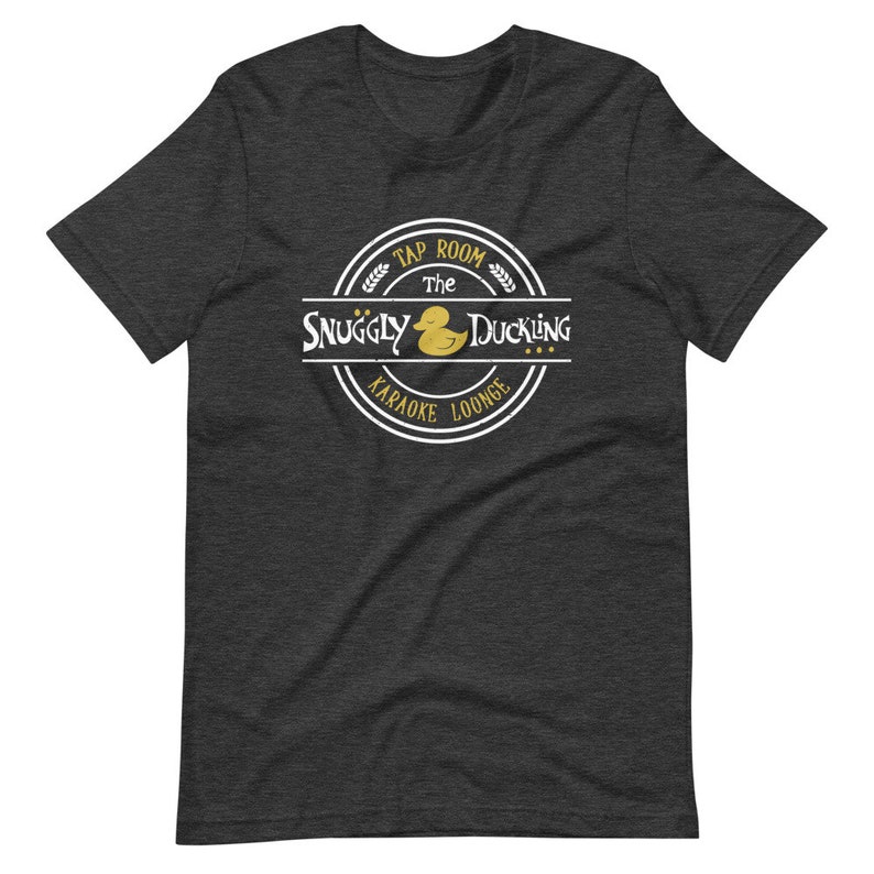May include: A dark heather grey t-shirt with a white circle logo featuring a yellow rubber duck and the text "The Snuggly Duckling Tap Room Karaoke Lounge".