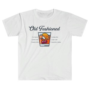 May include: White t-shirt with a graphic of an Old Fashioned cocktail recipe. The graphic includes a glass of the cocktail with a cherry, orange slice, and sugar cube. The text reads "Old Fashioned" and lists the ingredients: 2 oz brandy, 1 splash soda, 2 dashes bitters, 1 orange slice, 1 sugar cube, and 2 maraschino cherries.