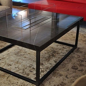 May include: A black marble coffee table with a black metal frame and a glass fire pit insert. The table is sitting on a rug.