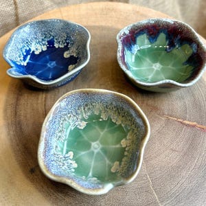 May include: Three small, ceramic bowls with a wavy rim. The bowls are glazed in shades of blue, green, and purple with a white crackle glaze.