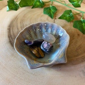 May include: A blue and brown ceramic seashell dish with four tumbled stones: a purple amethyst, a pink and black zebra stone, a brown tiger's eye, and a white agate.