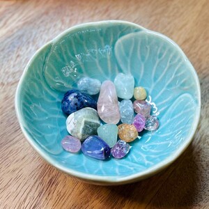 May include: A teal ceramic bowl filled with a variety of colourful tumbled stones, including pink, blue, green, and yellow.