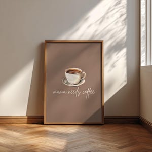 Könnte beinhalten: Ein gerahmter Kunstdruck mit einer weißen Keramik-Kaffeetasse auf einer Untertasse, zentriert auf einem einfarbigen, gedeckten braunen Hintergrund. Unter der Tasse steht der Text "mama needs coffee" in einer weißen, kursiven Handschrift.