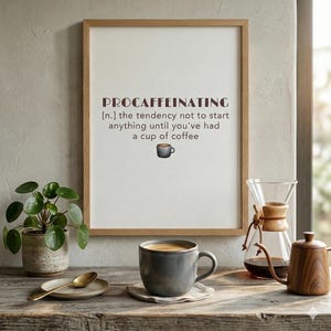 May include: A framed print with the word "PROCAFFEINATING" and a definition about needing coffee before starting tasks. A gray coffee mug sits on a coaster, with a plant and coffee brewing equipment in the background.