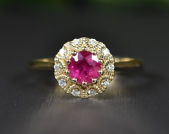 May include: A gold ring with a large, round, red ruby gemstone surrounded by a halo of smaller, white diamonds.