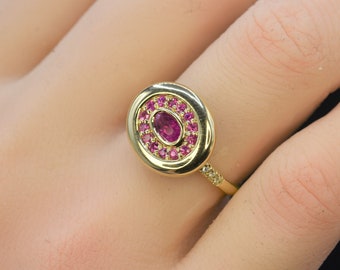 May include: A gold ring featuring a large oval-shaped pink gemstone surrounded by smaller pink gemstones. The ring has a thin band with small diamonds.