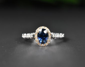 May include: A silver ring with a blue oval sapphire surrounded by a halo of smaller diamonds. The band is set with smaller diamonds.