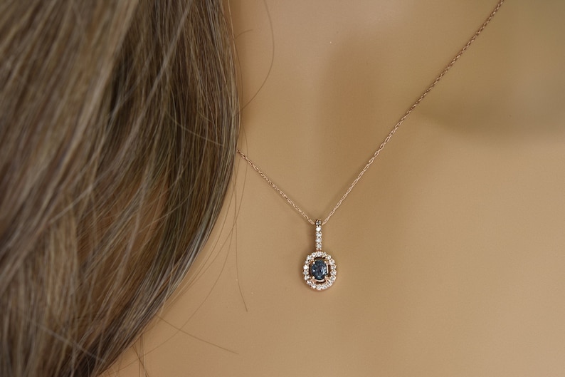 Puede incluir: Un delicado collar de oro rosa con un colgante que presenta una piedra ovalada azul oscuro rodeada por un halo de piedras transparentes m&aacute;s peque&ntilde;as.