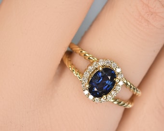 May include: A gold ring with a twisted band features a blue oval sapphire surrounded by a halo of smaller diamonds.