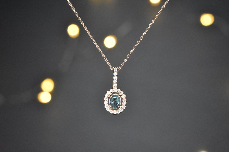 Puede incluir: Un delicado collar de oro con un colgante que presenta una piedra preciosa azul rodeada por un halo de diamantes m&aacute;s peque&ntilde;os.
