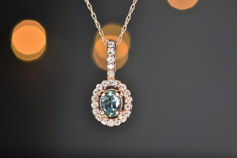 Puede incluir: Un delicado collar con un colgante en forma de gota de color verde rodeado por un halo de diamantes m&aacute;s peque&ntilde;os. El colgante est&aacute; suspendido de una fina cadena de oro.