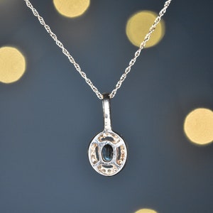 Puede incluir: Un collar de cadena de plata con un colgante que presenta una piedra ovalada azul oscura rodeada de piedras preciosas m&aacute;s peque&ntilde;as y transparentes.