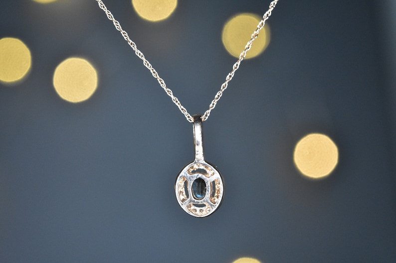 Puede incluir: Un collar de cadena de plata con un colgante que presenta una piedra ovalada azul oscura rodeada de piedras preciosas m&aacute;s peque&ntilde;as y transparentes.