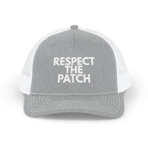 May include: A gray trucker hat with a white mesh back and a curved brim. The front of the hat features the white text "RESPECT THE PATCH". The hat has a snap closure for adjustable sizing.