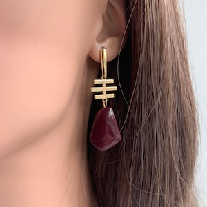 May include: Gold geometric dangle earrings with a burgundy teardrop-shaped stone.