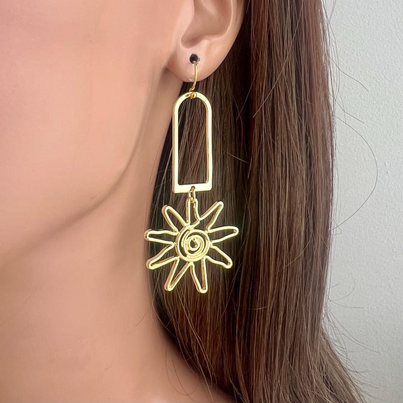 May include: Gold dangle earrings with a sun-shaped charm. The sun charm has a spiral design in the center.