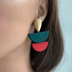 May include: A pair of geometric earrings with a teardrop-shaped top piece in cream, a half-circle in dark green, and a half-circle in red.