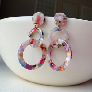 May include: A pair of colorful, multi-colored, multi-patterned, acrylic, dangle earrings with three linked circles. The circles are in a graduated size, with the largest circle at the bottom.